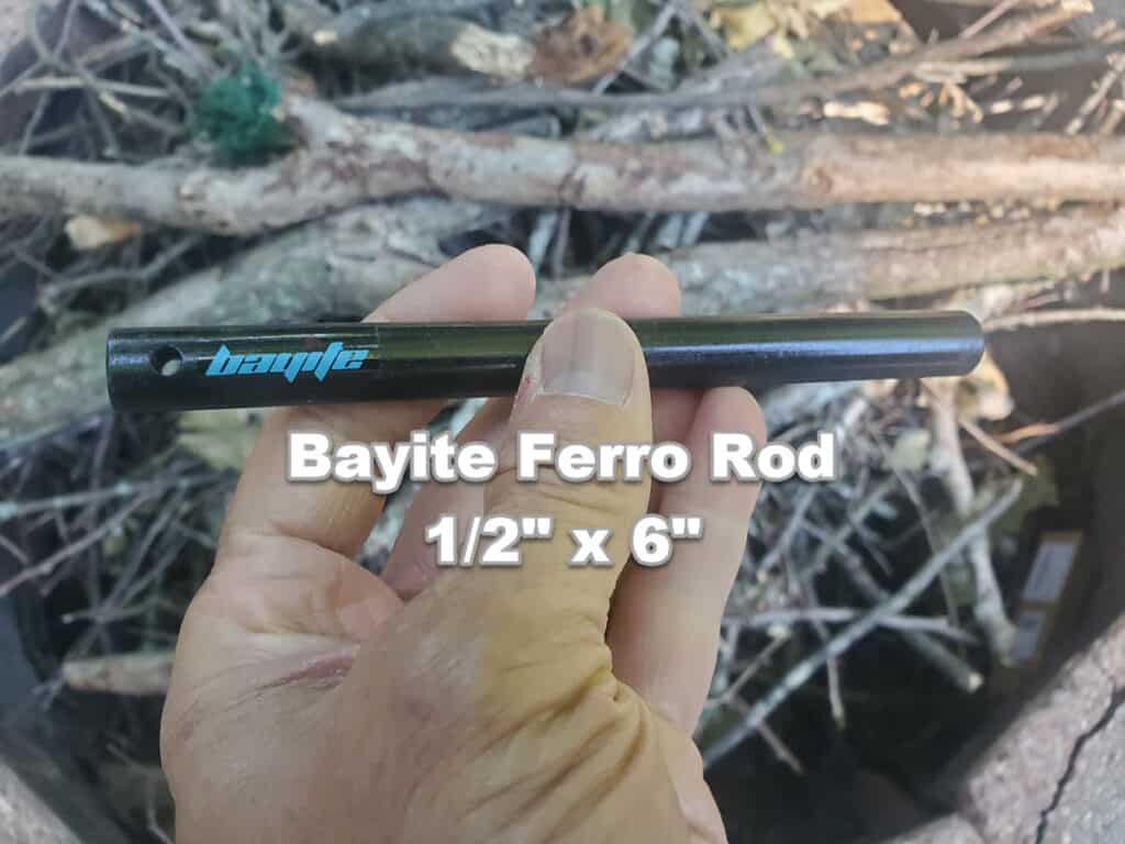 man holding 1/2 inch by 6 inches bayite ferro rod over fire pit