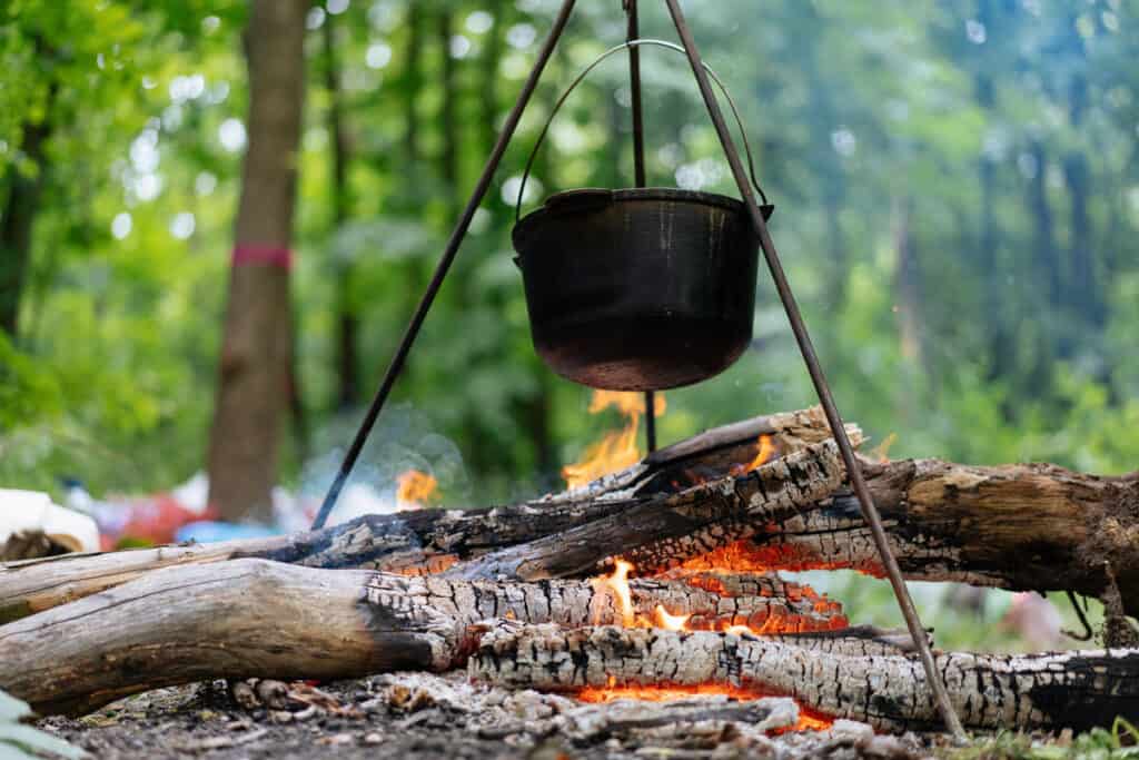 campfire with with black pot hanging from cooking tripod